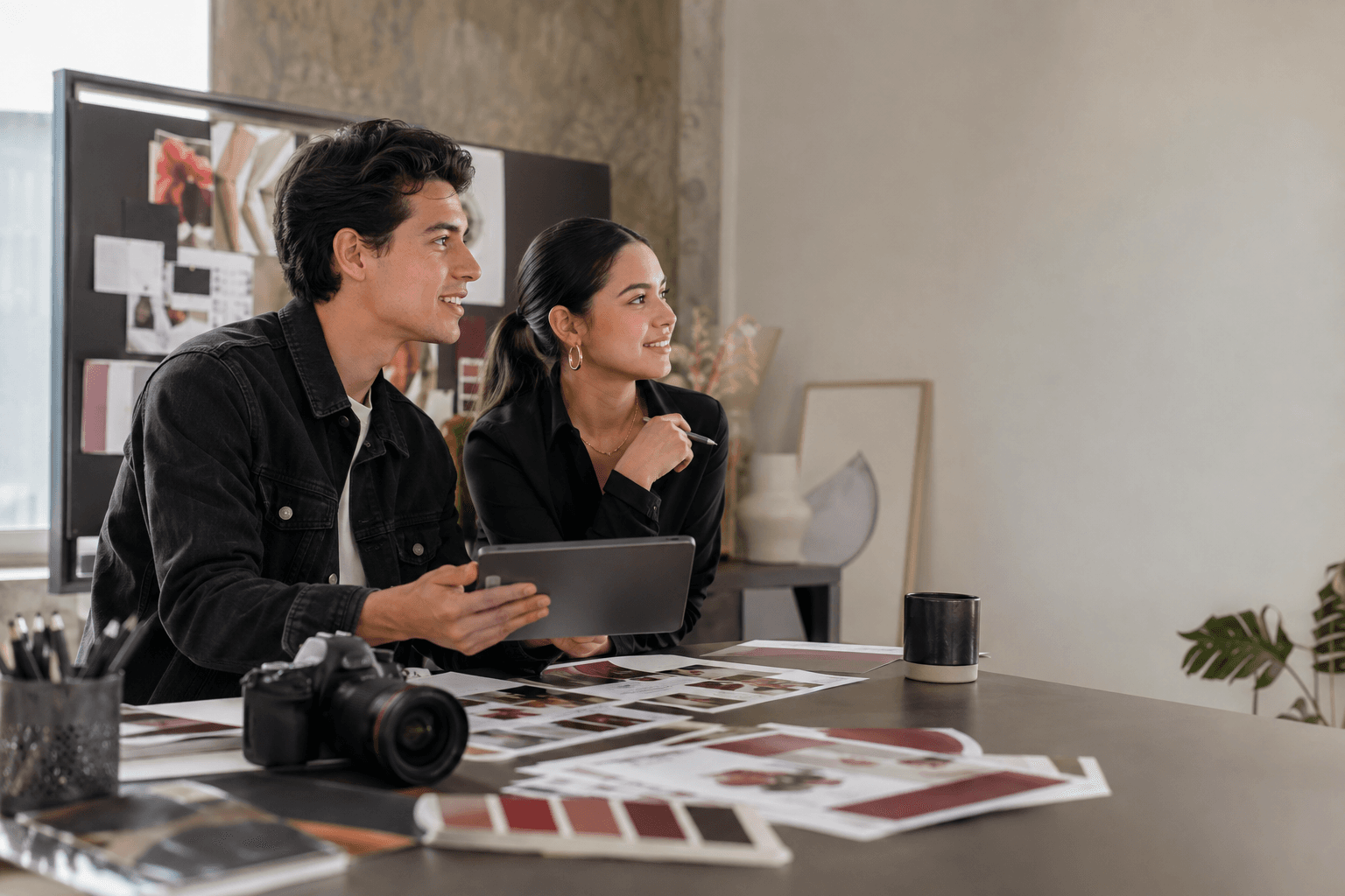 Dos profesionales de mercadotecnia revisan un moodboard de marca y bocetos de diseño en una tablet.